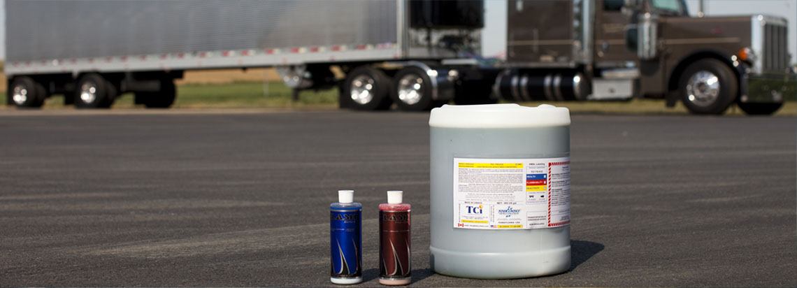 A container of Tetra-Chem and two bottles of Flash sitting on asphalt with an 18 wheeler in the background