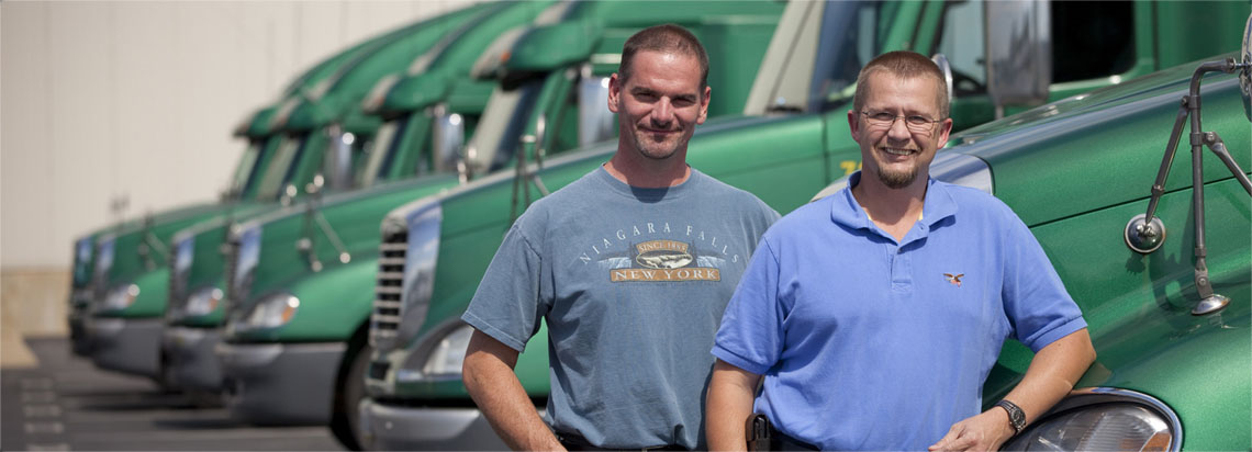 two men standing in front of several green truck cabs